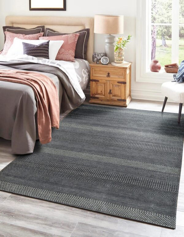 Dark gray rug with light patterned horizontal stripes under a bed on gray wood floors.