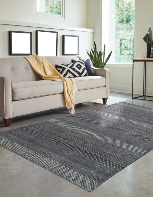 Gray rug featuring horizontal stripes of alternating geometric patterns anchors a light beige sofa.