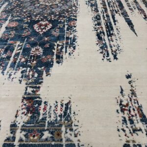 Cream rug featuring distressed navy floral patterns dissolving into abstract vertical streaks on light wood.