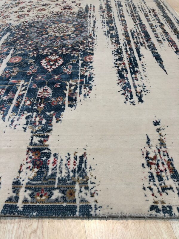 Cream rug featuring distressed navy floral patterns dissolving into abstract vertical streaks on light wood.