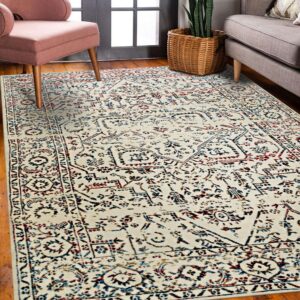 A distressed cream rug with traditional red and blue patterns sits on hardwood floors between pink and gray furniture.