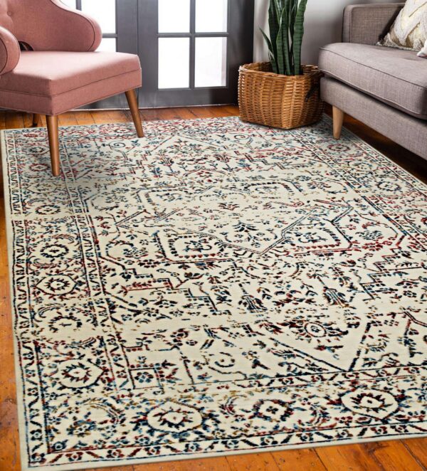 A distressed cream rug with traditional red and blue patterns sits on hardwood floors between pink and gray furniture.