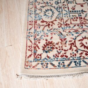 Cream rug with intricate red and blue traditional designs shown close-up on light blonde wood flooring.