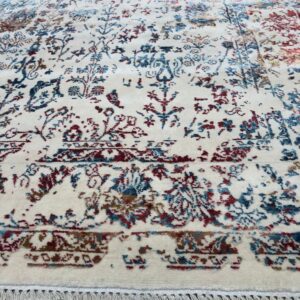 Ornate cream rug with faded floral designs in burgundy and teal, lying on light wood planks.
