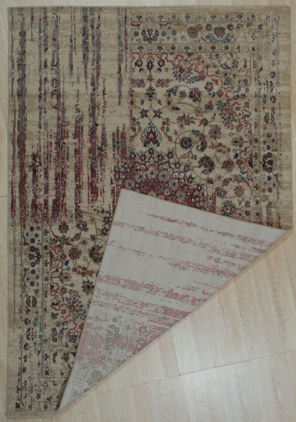 A beige transitional rug featuring red and blue patterns is flipped over on light plank flooring.