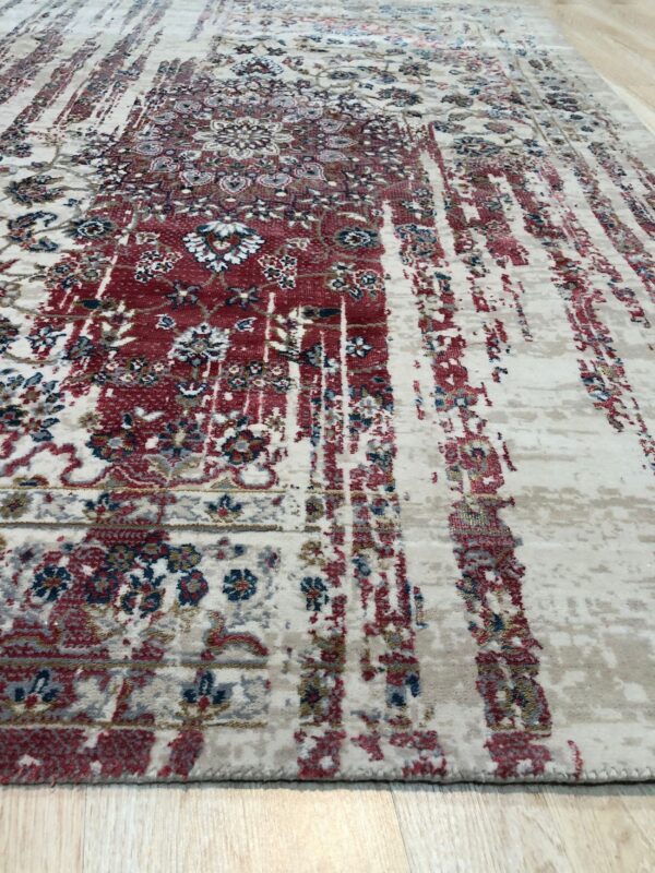 Cream rug with heavily distressed red, blue, and gray traditional patterns lying on light wood floors.