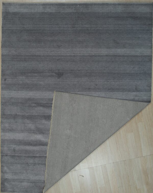 Textured gray rug featuring horizontal stripes and patterned bands, revealing a plain backing on light flooring.