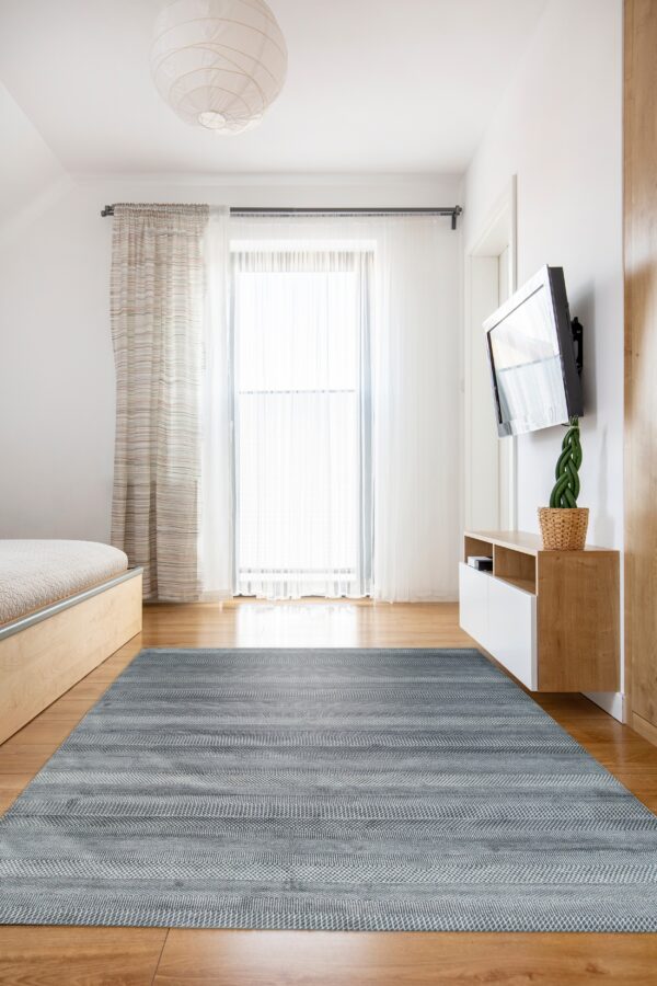 Gray and white striped flatweave rug on a light wood floor in a minimal bedroom setting.