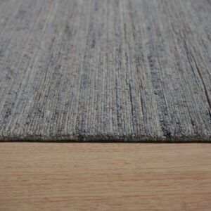 A close-up shows a ribbed blue-gray heathered rug resting on light wood plank flooring.
