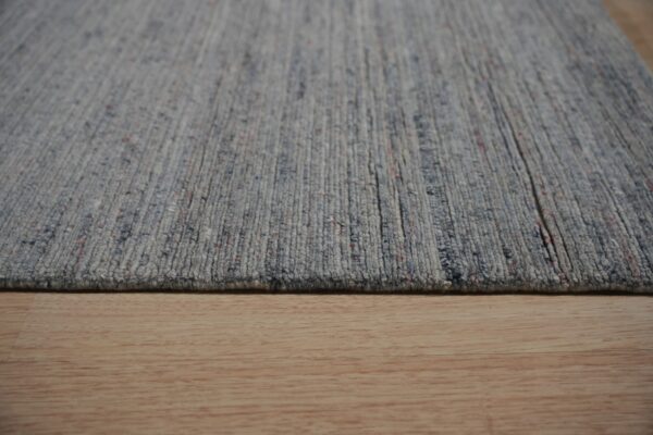 A close-up shows a ribbed blue-gray heathered rug resting on light wood plank flooring.
