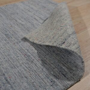Close-up of a ribbed blue-gray rug, showing the colorful flecked pile and rolled backing on light wood flooring.