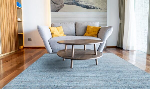 Low pile blue variegated rug anchors a gray sofa and dark wood table on polished hardwood flooring.