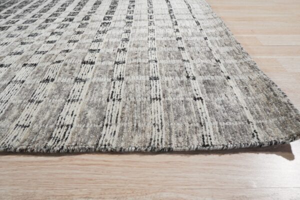 Textured gray rug with white vertical stripes and dark accents lying on light hardwood floor.