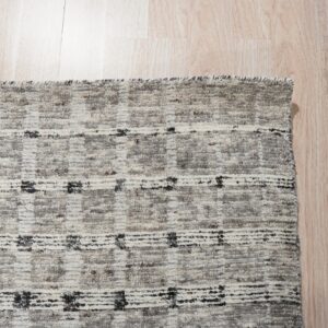 Textured gray rug with alternating checkered blocks and horizontal black stripes on light wood flooring.