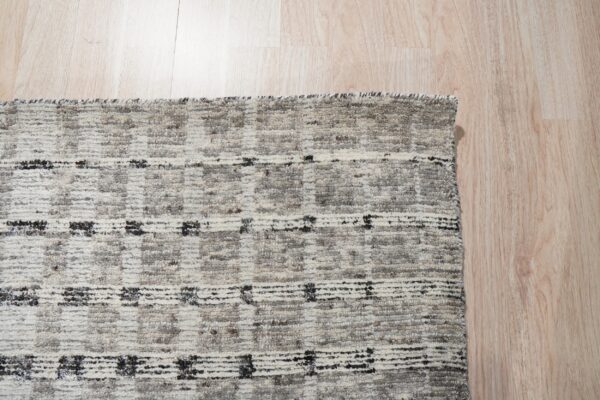 Textured gray rug with alternating checkered blocks and horizontal black stripes on light wood flooring.
