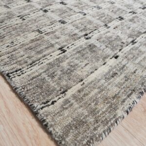 Corner view of a thick, shaggy gray rug featuring black and white abstract geometric lines on wood planks.