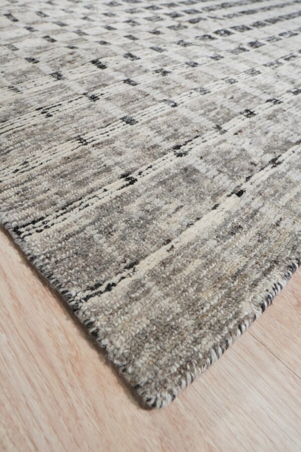Corner view of a thick, shaggy gray rug featuring black and white abstract geometric lines on wood planks.