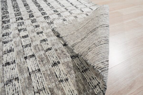Textured gray and off-white rug with a grid pattern, showing the woven backing on light wood floor.