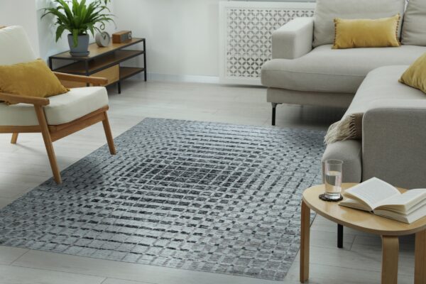 A gray abstract geometric rug defines a bright modern living room featuring light wood floors and neutral furniture.