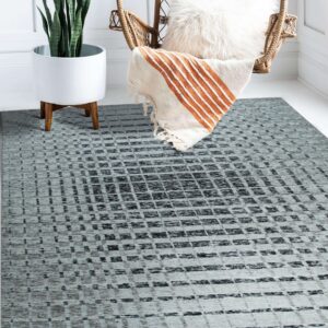 A gray and black distressed geometric rug rests on a white floor next to a rattan chair and snake plant.