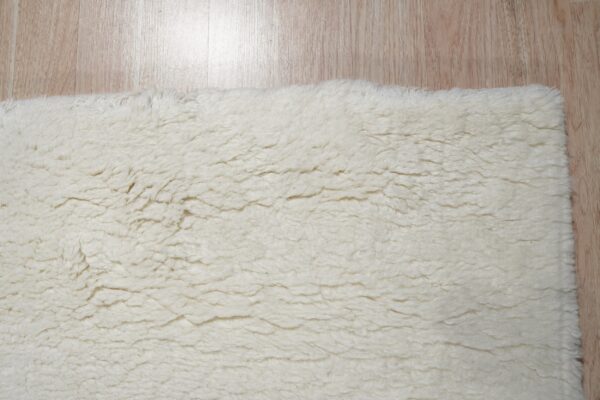 Creamy white high-pile shaggy rug shown close-up on a light wood plank floor.