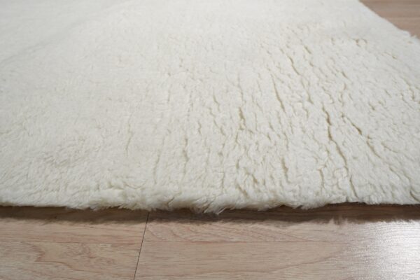 Thick, off-white, high-pile rug detail showing shaggy texture resting on light blonde wood flooring.
