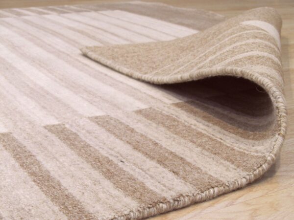 Beige and cream striped rug corner partially rolled back, showing medium pile on wood floor.