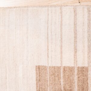 Textured cream rug with thick horizontal tan blocks and light vertical stripes on wood planks.