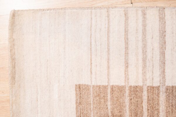 Textured cream rug with thick horizontal tan blocks and light vertical stripes on wood planks.