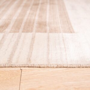 Close-up view of a pale beige striped rug border lying on light wood flooring.