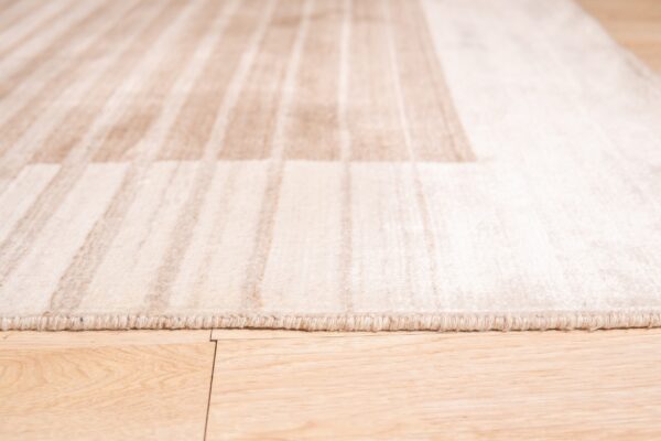 Close-up view of a pale beige striped rug border lying on light wood flooring.