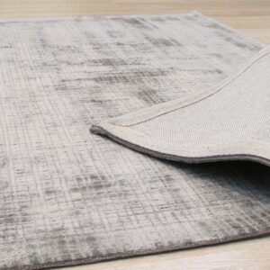 Light gray abstract rug on wood floor, with the woven backing revealed by a turned corner.