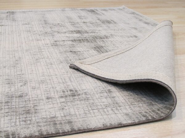 Light gray abstract rug on wood floor, with the woven backing revealed by a turned corner.