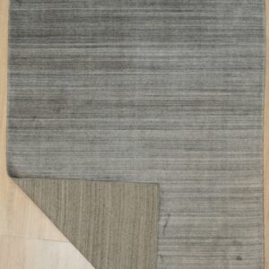 Low-pile gray rug with horizontal striations on light wood, corner flipped revealing the taupe backing.