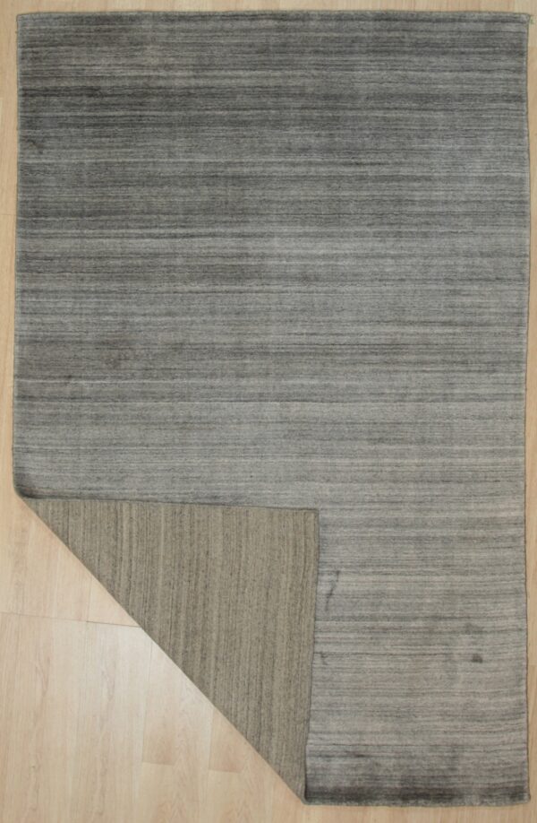 Low-pile gray rug with horizontal striations on light wood, corner flipped revealing the taupe backing.