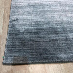 Dark gray ombre rug with horizontal stripes lying on light wood flooring.