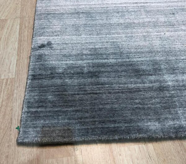 Dark gray ombre rug with horizontal stripes lying on light wood flooring.