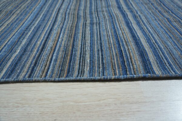 Low pile rug with thin vertical blue, tan, and gray stripes resting on pale wood floor.