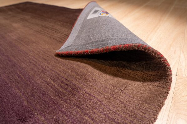 Low-pile brown and purple gradient rug is folded on a light wood floor.