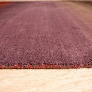 Low angle view of a dense, short-pile rug with maroon-to-tan stripes on light wood.