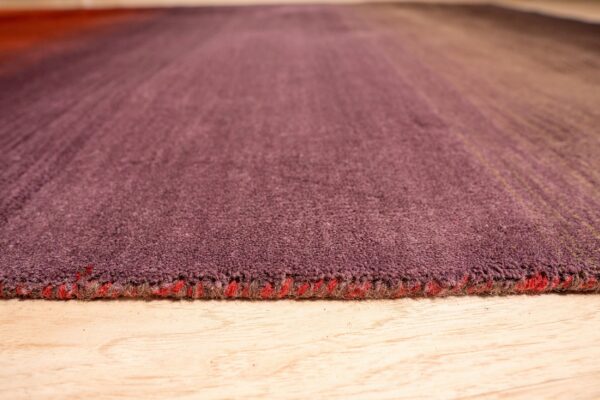 Low angle view of a dense, short-pile rug with maroon-to-tan stripes on light wood.