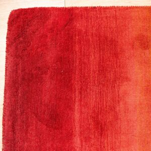 High-pile rug displaying a red to orange ombre gradient on light wood plank flooring.