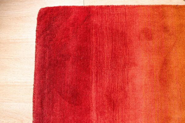 High-pile rug displaying a red to orange ombre gradient on light wood plank flooring.