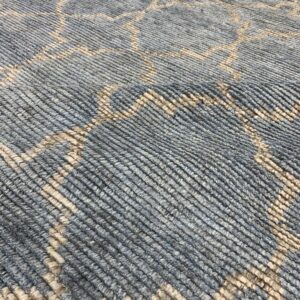 Muted blue-gray rug features a light beige geometric pattern and visible thick, ribbed texture.