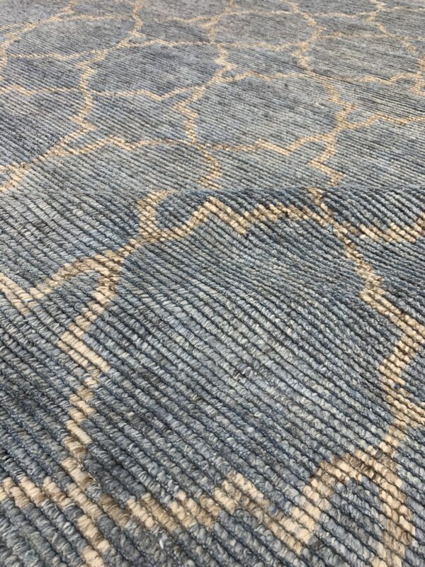 Muted blue-gray rug features a light beige geometric pattern and visible thick, ribbed texture.