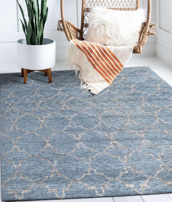 Low-pile blue trellis rug anchors a corner with a wicker chair, throw blanket, and snake plant.