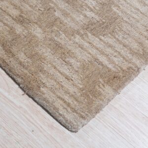 A corner of a textured beige rug with subtle stripes rests on pale wood plank flooring.