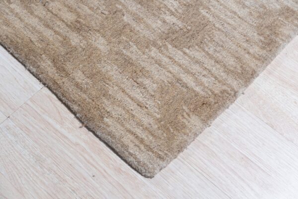 A corner of a textured beige rug with subtle stripes rests on pale wood plank flooring.