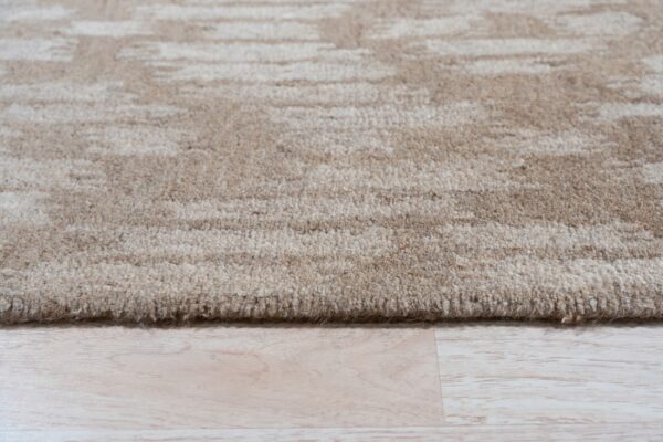A textured beige rug with subtle abstract striping lies on pale wood plank flooring.