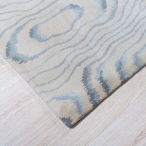 Light beige and gray plush rug with an abstract wavy pattern on bright blonde wood plank flooring.